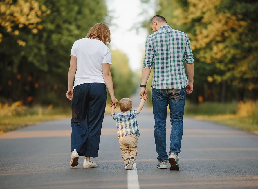 Young family walking hand in hand on a tree-lined road, symbolizing secure future from Estate planning attorney in Austin
